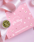 Pink 'Oh Flossy' makeup and glitter set with a small container of gold glitter on a pink background.