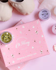 Makeup and glitter set with 'Oh Flossy' branding on a pink background