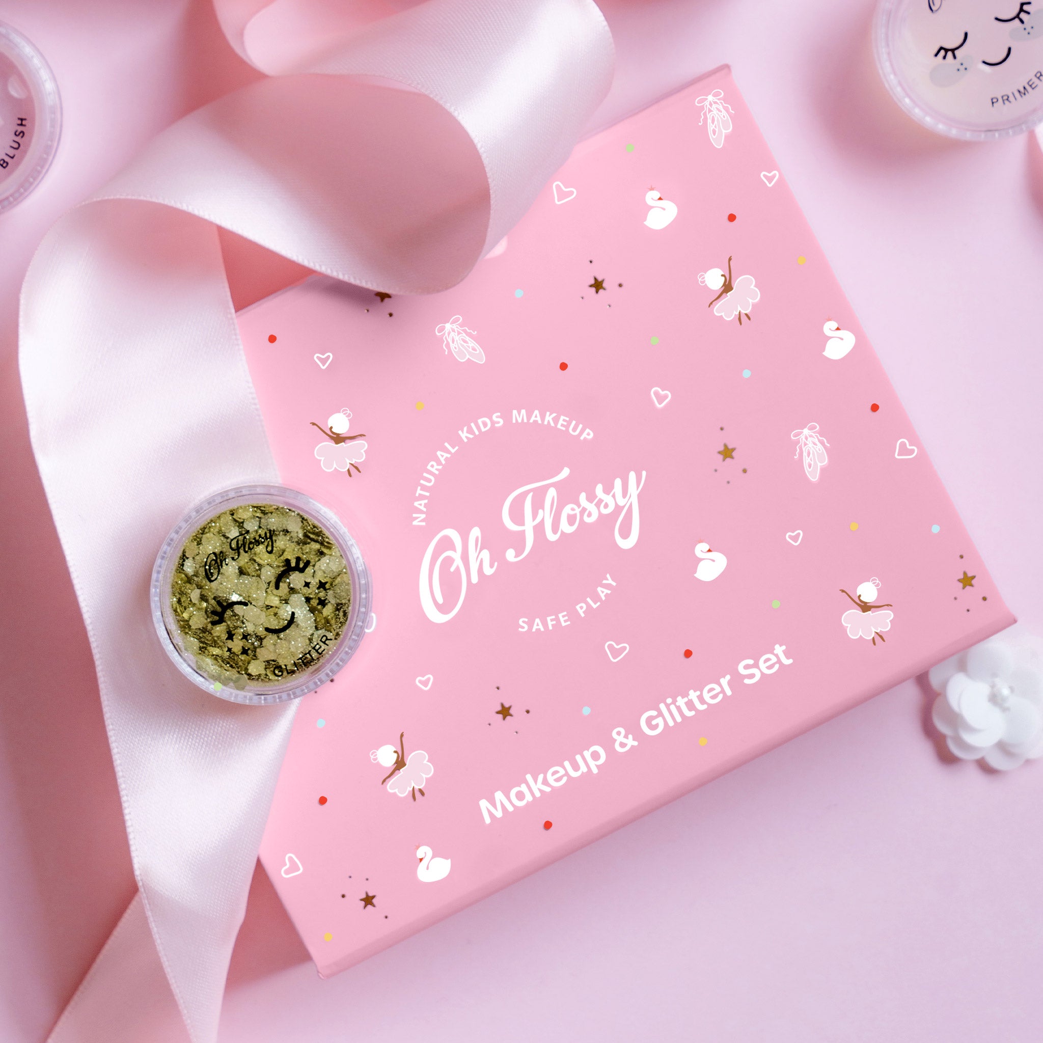 Pink 'Oh Flossy' makeup and glitter set with a small container of gold glitter on a pink background.