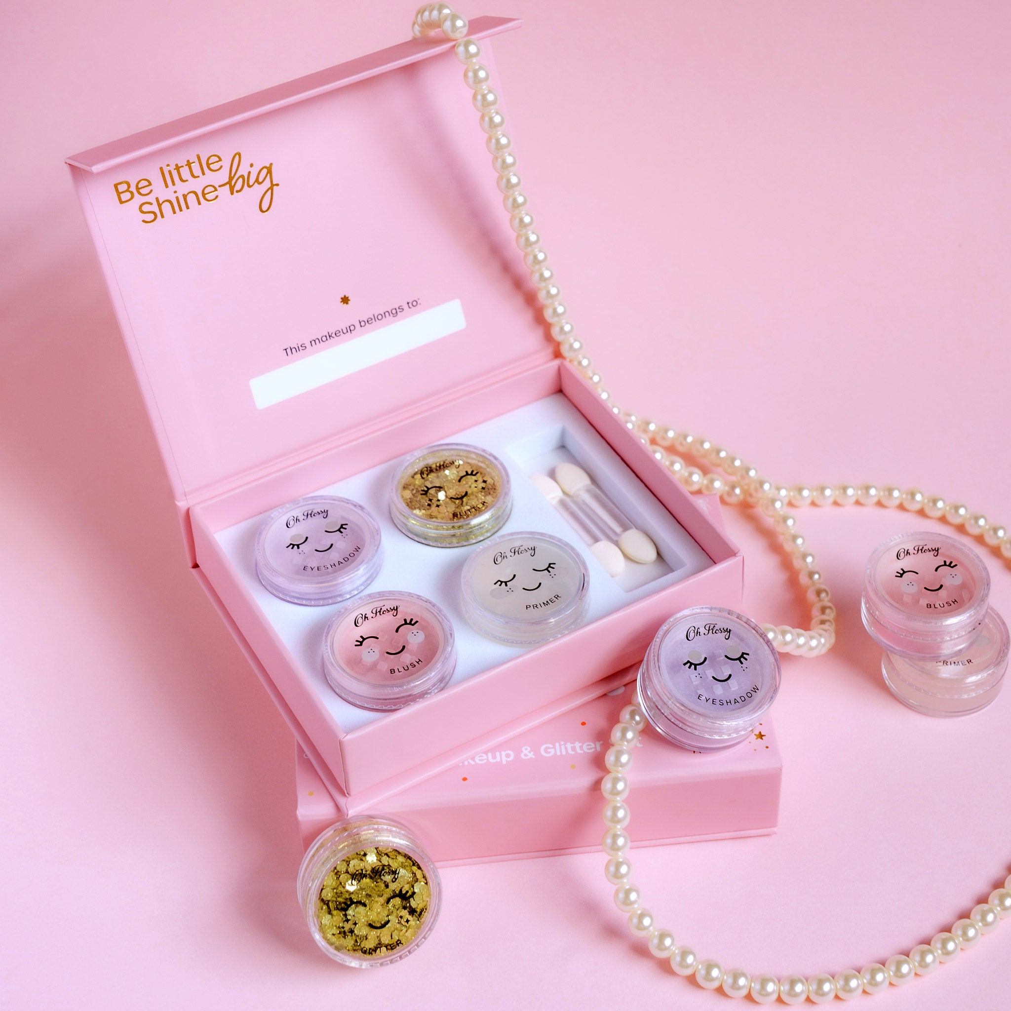 Makeup set with small jars and applicators in a pink box on a pink background