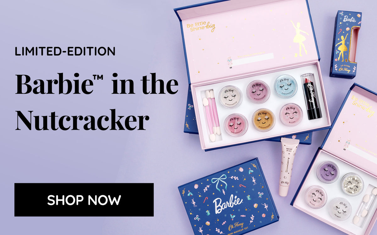 A Barbie-themed kids make-up gift set arranged on a light lavender background, including open pink and blue boxes with eyeshadows, glitter, blush, lipstick, lip gloss and prime with a text reading 'Limited-edition Barbie in the Nutcracker' and a button that says 'Shop Now'.